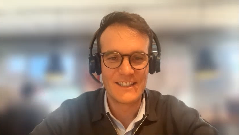 Dr. Pierre Baque with headset, blurred background, during interview.